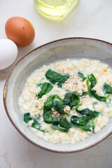 Bowl of stracciatella or egg-drop soup with spinach, vertical shot on a light-beige marble background, middle close-up, selective focus