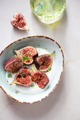 Green bowl with greek yogurt and fresh torn figs, vertical shot on a beige granite background, high angle view