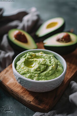 Homemade organic guacamole dip, sauce or spread made of ripe mashed avocado served in glass bowl  on cutting board on gray background