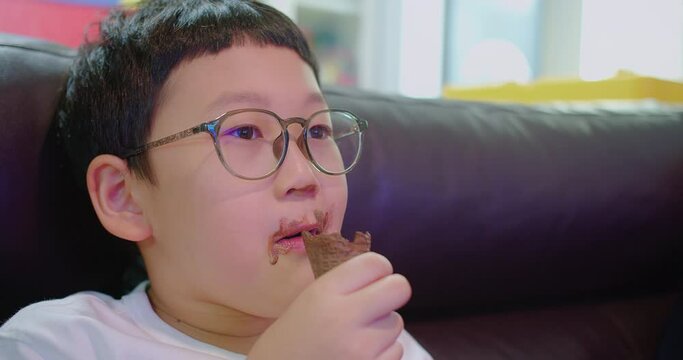 A young child with glasses enjoys a chocolate ice cream cone, with traces of dessert on their face, depicting a moment of innocent indulgence.