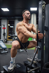 Fototapeta na wymiar Concentrated muscular man in black shorts, doing squats with weight, training in modern gym. Low angle view of male Caucasian bodybuilder exercising at evening time. Concept of bodybuilding, crossfit.