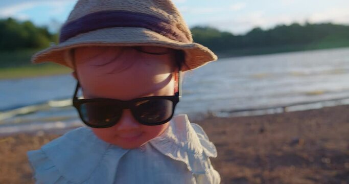 Toddler in straw hat and sunglasses at the lakeside, embodying summer joy with a playful smirk during golden hour
