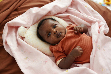 Portrait of adorable Black baby lying on bed wrapped in soft blanket