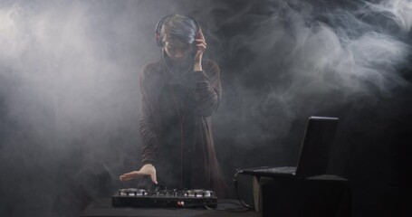 Smoke haze and female DJ on a mixer. Girl playing trance music. Fog and beam of lights in the background.