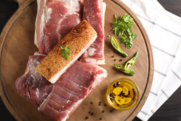 Pieces of raw pork belly, chili pepper, peppercorns, oil and parsley on black wooden table, top view