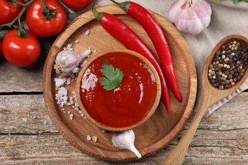 Delicious ketchup in bowl, products and spices on wooden table, flat lay. Tomato sauce