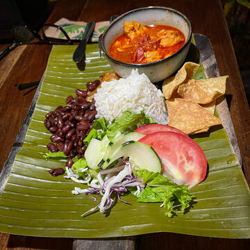A traditional Costa Rican dish known as Casado comprises rice, black beans, plantains, salad, a tortilla, and chicken stew providing the protein, all served atop a banana tree leaf at a soda eatery