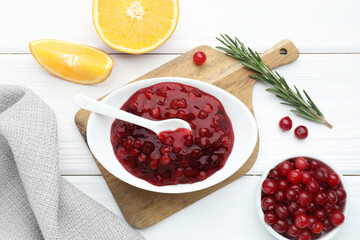 Tasty cranberry sauce in bowl, fresh berries, orange slices and rosemary on white wooden table, flat lay