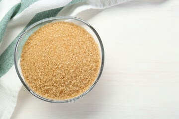 Brown sugar in glass bowl on white wooden table, top view. Space for text
