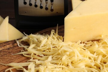 Grated and whole piece of cheese on wooden board, closeup