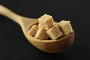 Brown sugar cubes in spoon on black table, closeup
