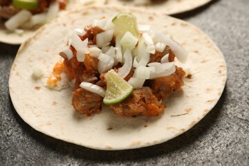 Delicious tacos with vegetables, meat and lime on grey textured table, closeup