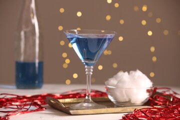 Tasty cocktail and cotton candy on white table against beige background with blurred lights, closeup