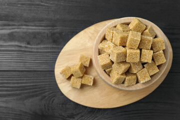 Brown sugar cubes in bowl on black wooden table, top view. Space for text