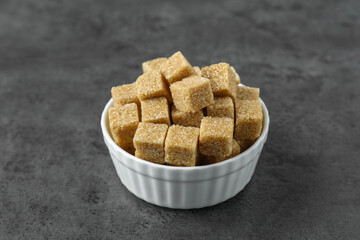 Brown sugar cubes in bowl on grey table