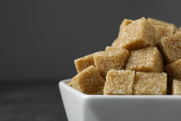 Brown sugar cubes in bowl on grey background, closeup. Space for text