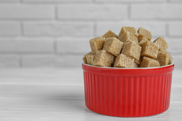Brown sugar cubes in bowl on white wooden table, closeup. Space for text