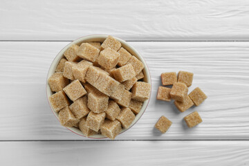 Brown sugar cubes in bowl on white wooden table, top view