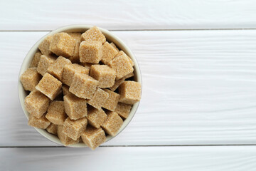 Brown sugar cubes in bowl on white wooden table, top view. Space for text
