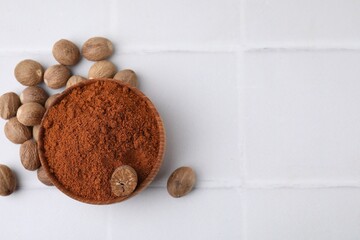 Nutmeg powder in bowl and seeds on white tiled table, flat lay. Space for text
