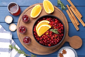 Cranberries in bowl, jars with sauce and ingredients on blue wooden table, flat lay
