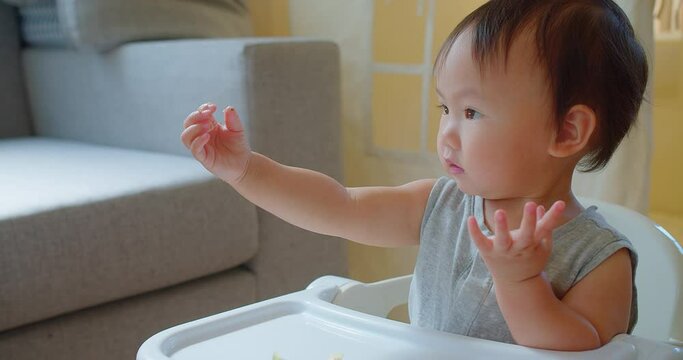 A cheerful toddler enjoys mealtime in a high chair, reaching out towards food with a bright, engaging smile in a sunny home