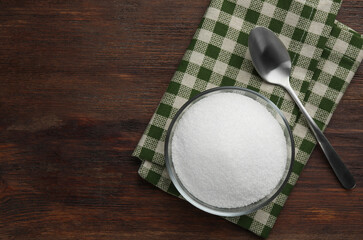 Granulated sugar in bowl, spoon and napkin on wooden table, top view. Space for text