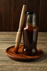 Tasty barbeque sauce in bottle and brush on wooden table