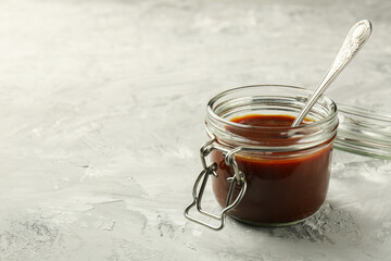 Tasty barbeque sauce in jar on grey textured table, closeup. Space for text