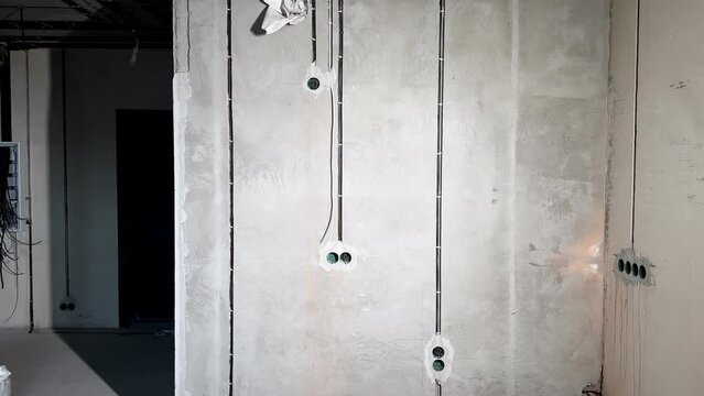 Wires, cables in grey concrete walls, socket places during rough electricity works, repair, house renovation
