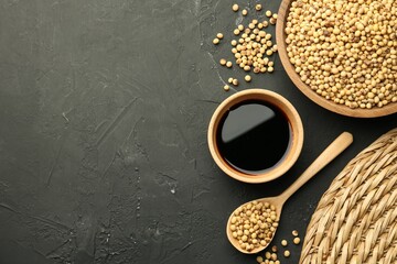 Soy sauce in bowl and soybeans on black textured table, flat lay. Space for text