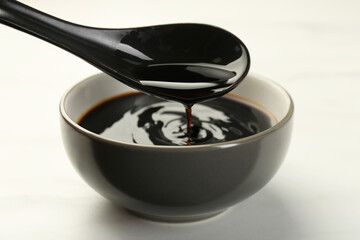 Taking soy sauce with spoon from bowl at white table, closeup