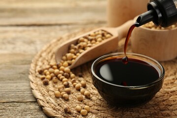 Pouring soy sauce into bowl at wooden table, closeup. Space for text