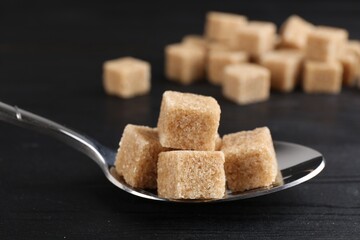 Brown sugar cubes in spoon on black wooden table, closeup