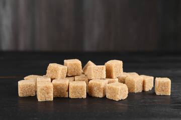 Many brown sugar cubes on black wooden table, closeup
