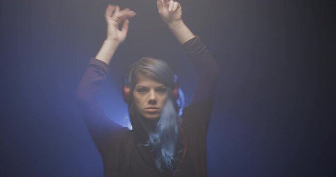 Girl with blue hair and red headphones. Portrait of a lady dancing. Blue beam of light and smoke in the backgorund. Slow motion video recorded at 50fps