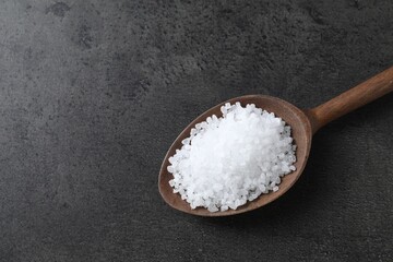 Fototapeta na wymiar Natural salt in wooden spoon on dark grey table, top view. Space for text