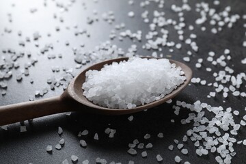 Natural salt and wooden spoon on black table, closeup