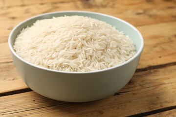 Raw basmati rice in bowl on wooden table, closeup