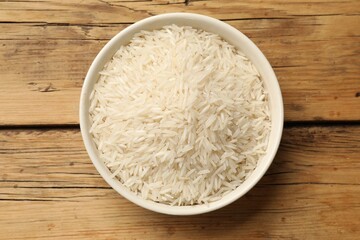 Raw basmati rice in bowl on wooden table, top view