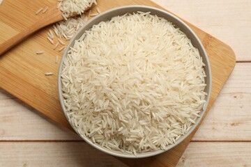Raw basmati rice in bowl on white wooden table, top view
