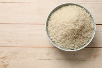 Raw basmati rice in bowl on white wooden table, top view. Space for text