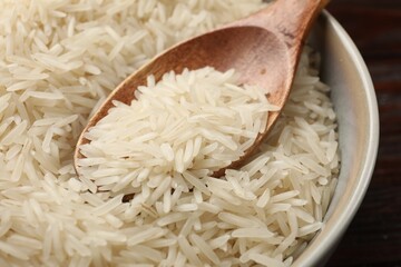 Raw basmati rice and wooden spoon in bowl on table, closeup