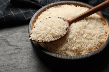 Raw basmati rice in bowl and spoon on black table, closeup
