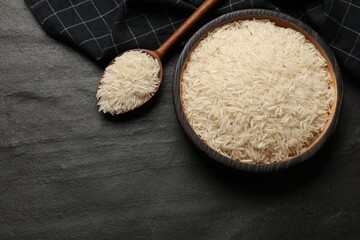 Raw basmati rice in bowl and spoon on black table, top view. Space for text
