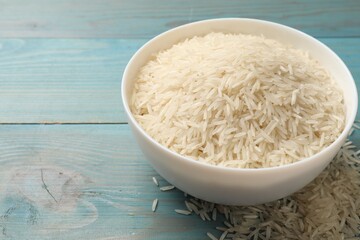 Raw basmati rice in bowl on light blue wooden table, space for text