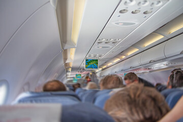 Rear view of the interior of the plane filled with tourists sitting on the seats. The photo...