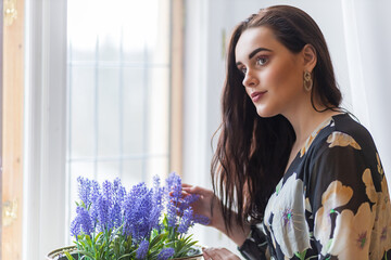 Portrait of beautiful dark long haired girl is holding  purple flowers in a pot. Horizontally. 