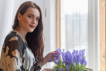 Portrait of beautiful smiling dark long haired girl is holding  purple flowers in a pot. Horizontally. 