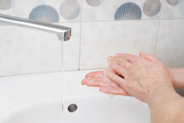 Washing hands with liquid soap in a bottle under the faucet in the bathroom. An image on the theme...